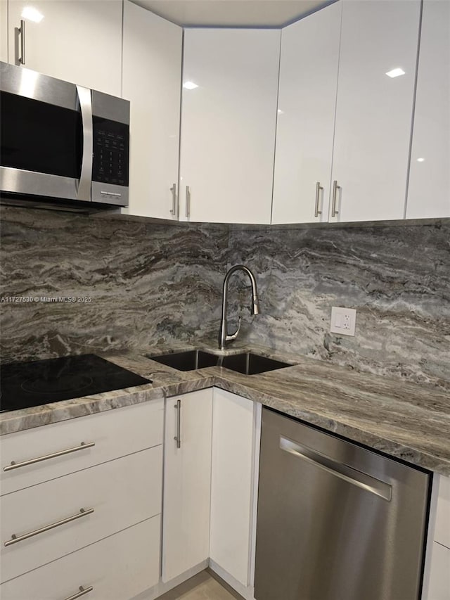 kitchen with sink, appliances with stainless steel finishes, dark stone countertops, backsplash, and white cabinets