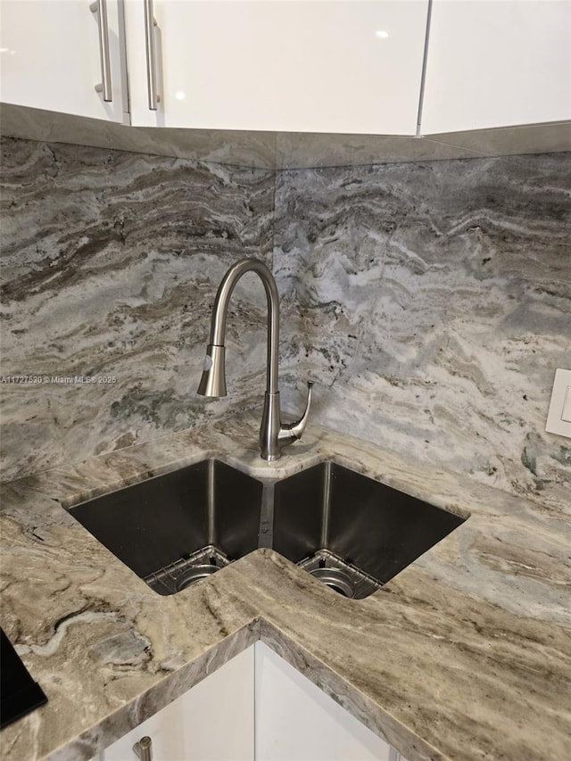 details with tasteful backsplash, white cabinetry, sink, and stone counters