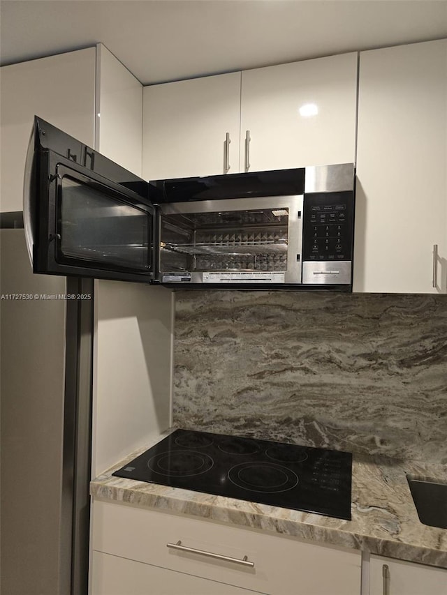 kitchen with light stone counters, black electric stovetop, decorative backsplash, and white cabinets