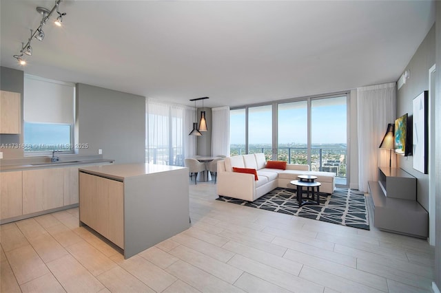 kitchen with sink, hanging light fixtures, floor to ceiling windows, a kitchen island, and light brown cabinetry