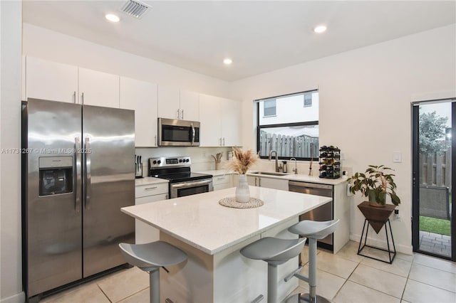 kitchen with a kitchen island, appliances with stainless steel finishes, white cabinetry, sink, and a breakfast bar area