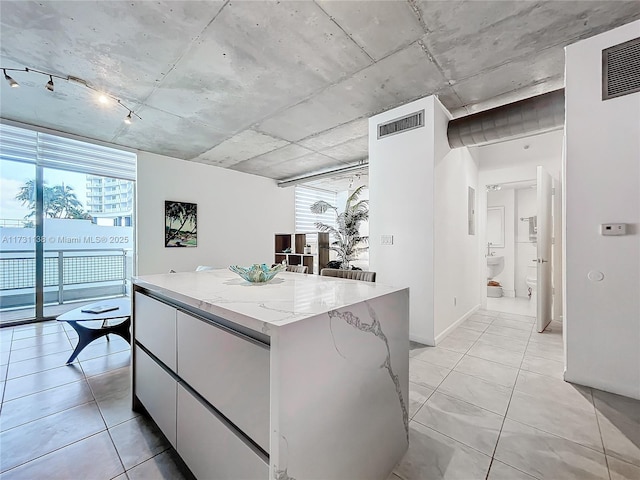 kitchen featuring track lighting, light stone countertops, white cabinets, and a kitchen island