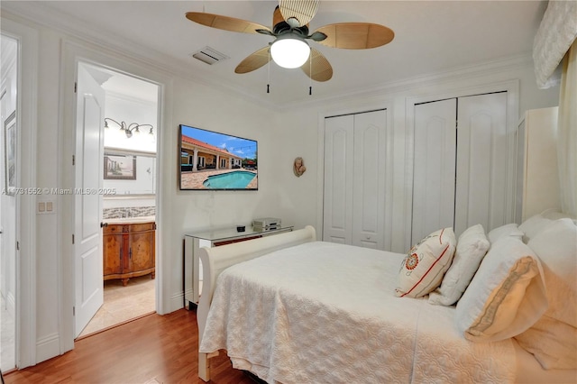 bedroom with two closets, ornamental molding, light hardwood / wood-style floors, and ceiling fan