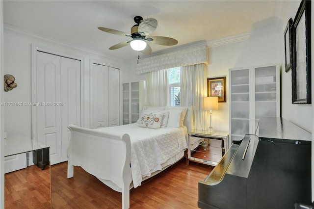 bedroom featuring ceiling fan, wood finished floors, ornamental molding, and two closets