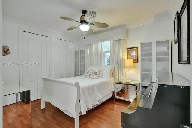 bedroom featuring hardwood / wood-style flooring, ceiling fan, crown molding, and two closets