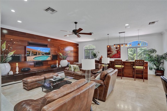 living room with plenty of natural light, ornamental molding, wooden walls, and ceiling fan