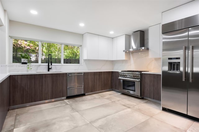 kitchen featuring wall chimney exhaust hood, dark brown cabinetry, sink, high quality appliances, and white cabinets