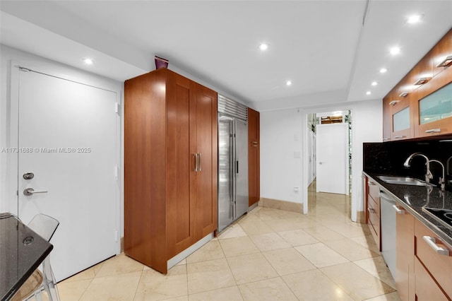 kitchen with sink, dark stone countertops, stainless steel built in refrigerator, light tile patterned flooring, and decorative backsplash