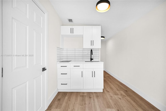 bar with light wood-style flooring, a sink, visible vents, baseboards, and decorative backsplash