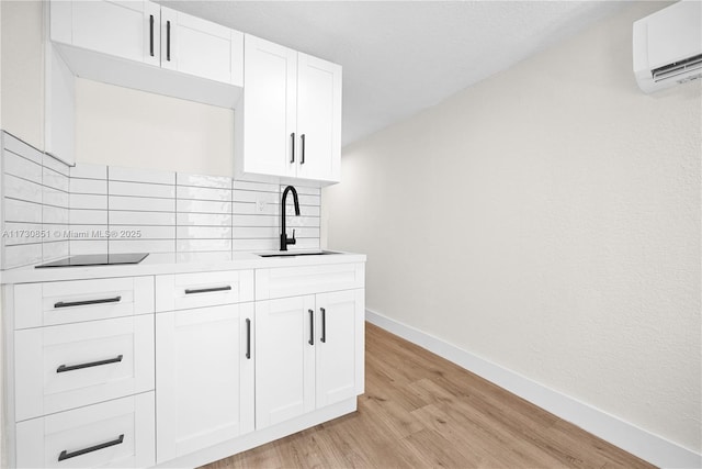 kitchen with sink, white cabinetry, a wall unit AC, black electric stovetop, and light hardwood / wood-style floors