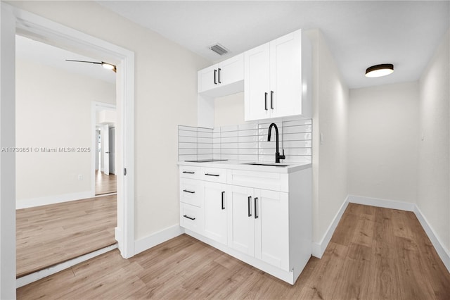 kitchen featuring visible vents, a sink, backsplash, and light wood finished floors