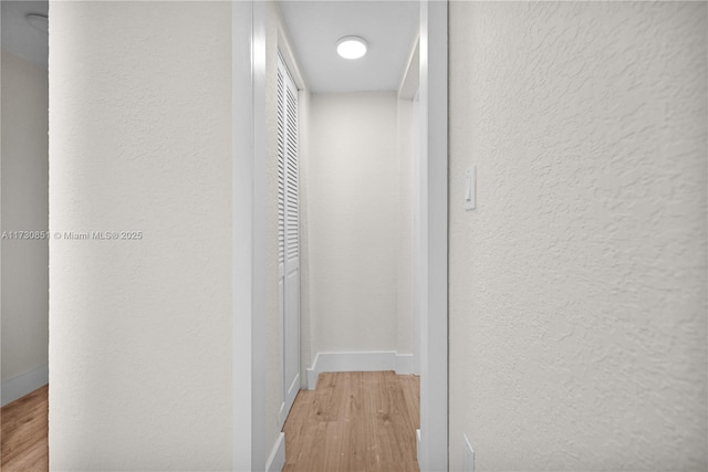 hall featuring a textured wall, wood finished floors, and baseboards