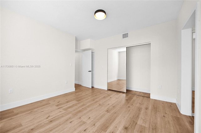 unfurnished bedroom with light wood-type flooring, baseboards, visible vents, and a closet