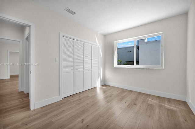 unfurnished bedroom with light wood finished floors, a closet, visible vents, and baseboards