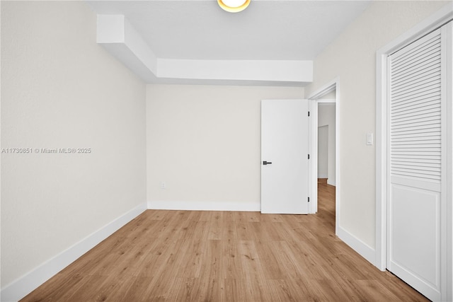 unfurnished bedroom featuring light wood-type flooring, baseboards, and a closet