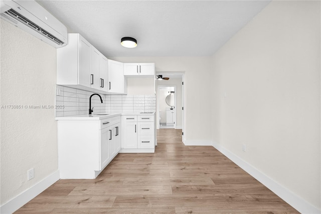 kitchen featuring a sink, light wood-style floors, light countertops, decorative backsplash, and a wall mounted air conditioner