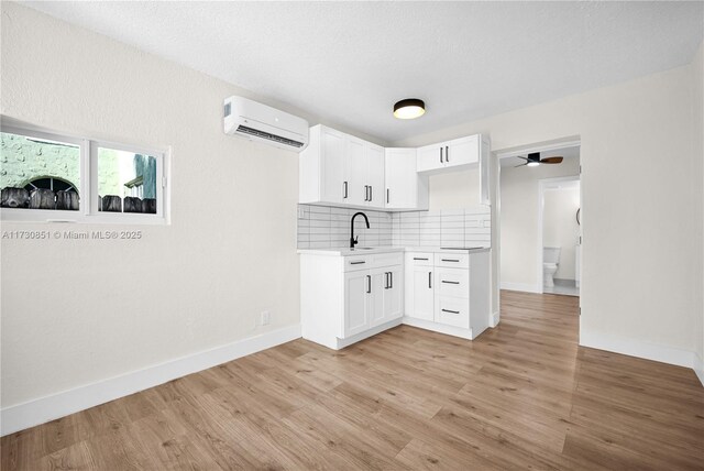 kitchen featuring sink, white cabinetry, light hardwood / wood-style floors, decorative backsplash, and an AC wall unit