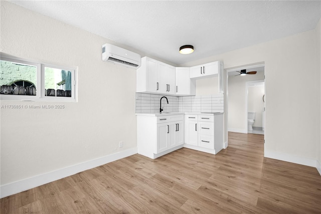 kitchen featuring a wall unit AC, light wood-style floors, tasteful backsplash, and light countertops