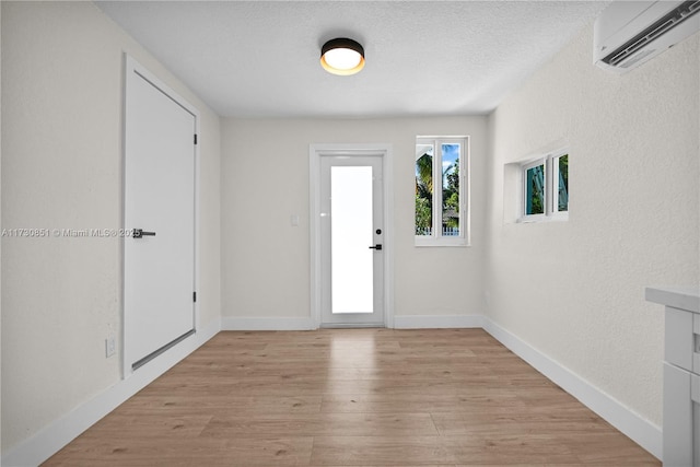 foyer entrance with an AC wall unit, baseboards, light wood-style flooring, and a textured ceiling