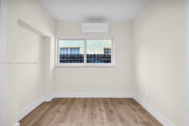 unfurnished room with an AC wall unit, wood finished floors, and baseboards