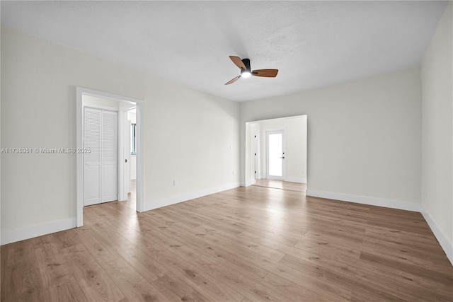 empty room with a ceiling fan, light wood-style flooring, baseboards, and a textured ceiling