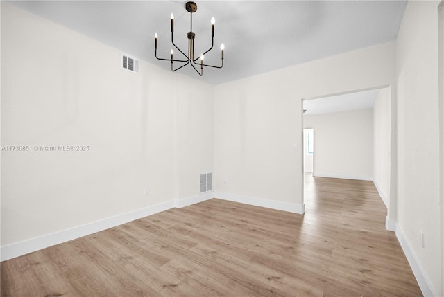 unfurnished room featuring a notable chandelier, wood finished floors, visible vents, and baseboards