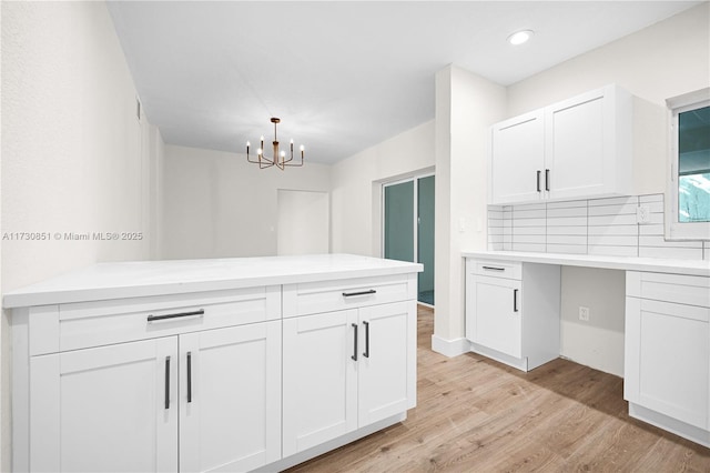 kitchen with white cabinets, light wood finished floors, light countertops, hanging light fixtures, and tasteful backsplash