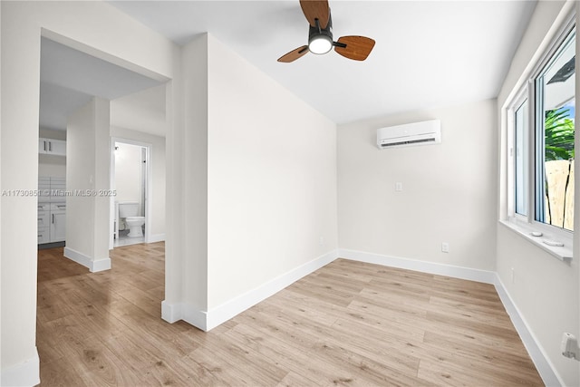 empty room with a ceiling fan, an AC wall unit, light wood-style flooring, and baseboards