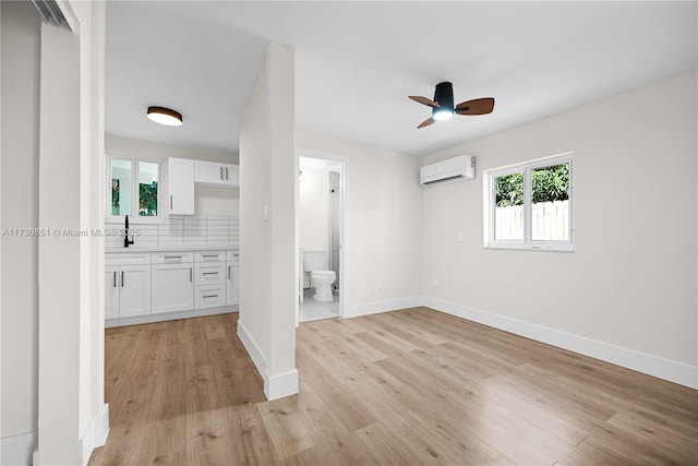 interior space with light wood-style floors, baseboards, a ceiling fan, and a wall mounted air conditioner