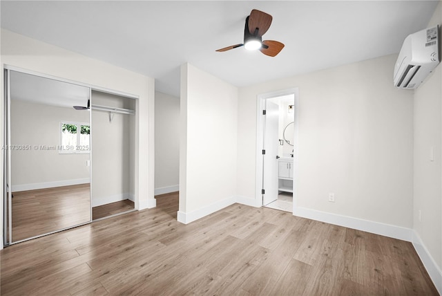 unfurnished bedroom featuring a wall unit AC, light wood finished floors, a closet, ensuite bathroom, and baseboards