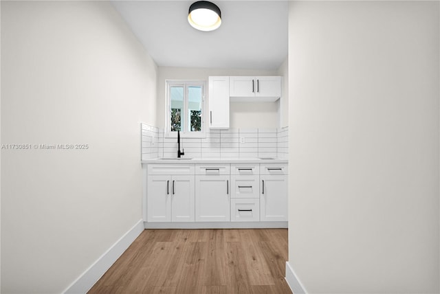 bar featuring light wood-style flooring, a sink, backsplash, and baseboards