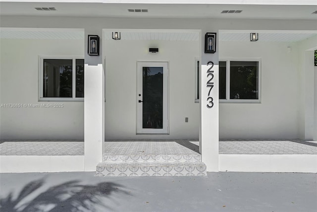 view of exterior entry with covered porch, visible vents, and stucco siding