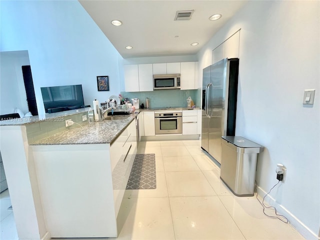 kitchen with light tile patterned flooring, appliances with stainless steel finishes, sink, white cabinets, and kitchen peninsula