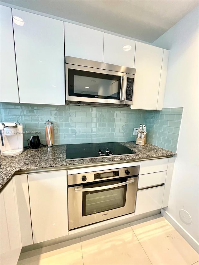 kitchen featuring white cabinetry, dark stone countertops, backsplash, light tile patterned floors, and stainless steel appliances