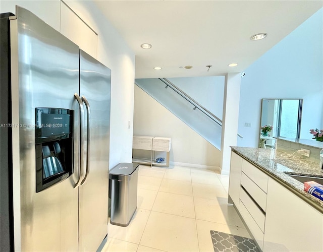 kitchen featuring white cabinetry, stainless steel fridge, light tile patterned floors, and stone counters