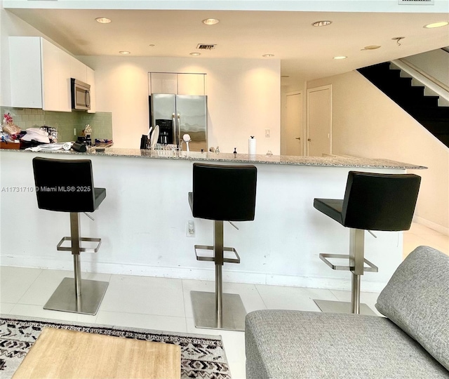 kitchen featuring a breakfast bar, white cabinetry, tasteful backsplash, light tile patterned floors, and stainless steel appliances