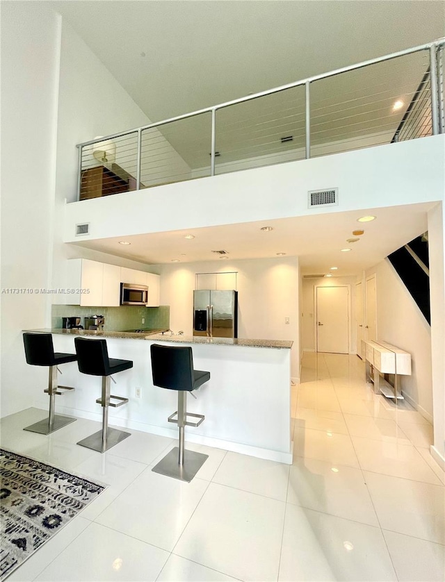 kitchen with appliances with stainless steel finishes, a towering ceiling, white cabinetry, light tile patterned floors, and kitchen peninsula