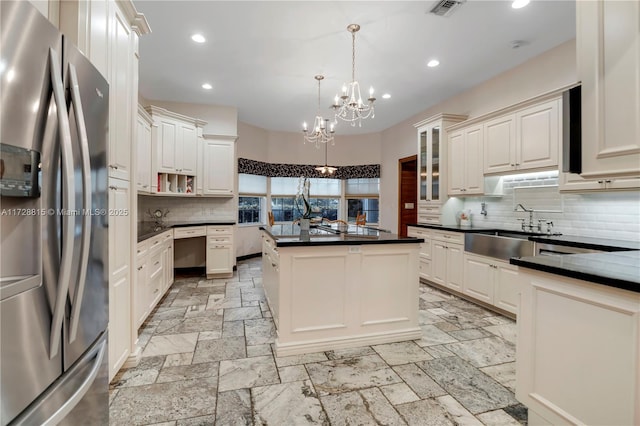 kitchen with sink, stainless steel fridge, backsplash, a kitchen island, and decorative light fixtures