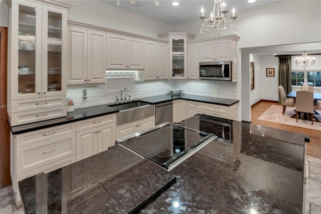 kitchen with appliances with stainless steel finishes, decorative light fixtures, white cabinetry, sink, and a notable chandelier