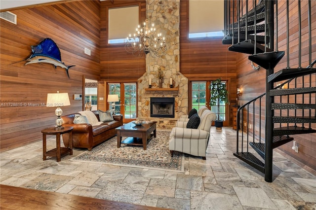 living room featuring an inviting chandelier, a towering ceiling, a fireplace, and wooden walls