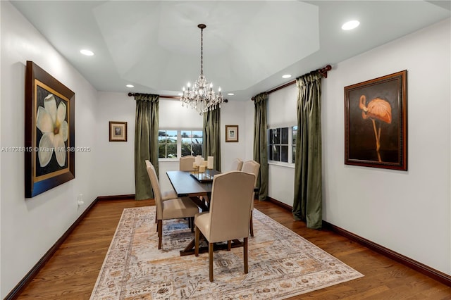 dining area with an inviting chandelier, a tray ceiling, and wood-type flooring