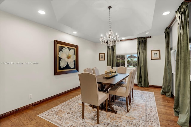 dining area with a tray ceiling, a chandelier, and light wood-type flooring