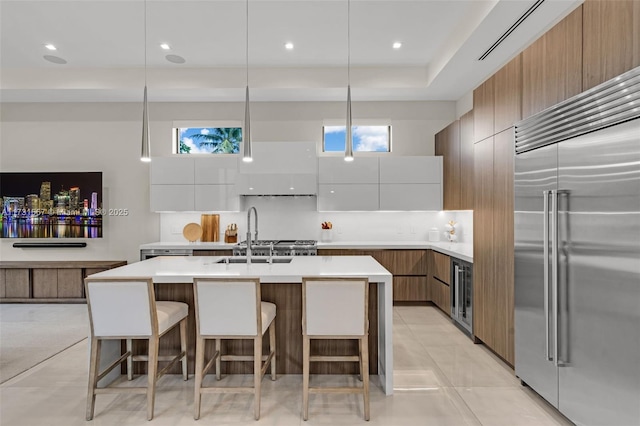 kitchen featuring pendant lighting, sink, a kitchen breakfast bar, stainless steel built in refrigerator, and white cabinets