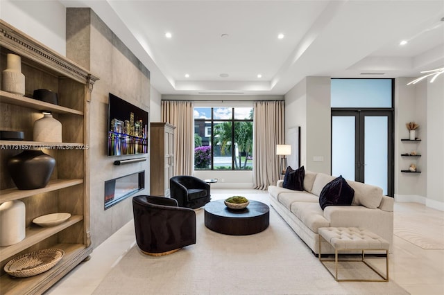 living room featuring a tiled fireplace, french doors, and a raised ceiling