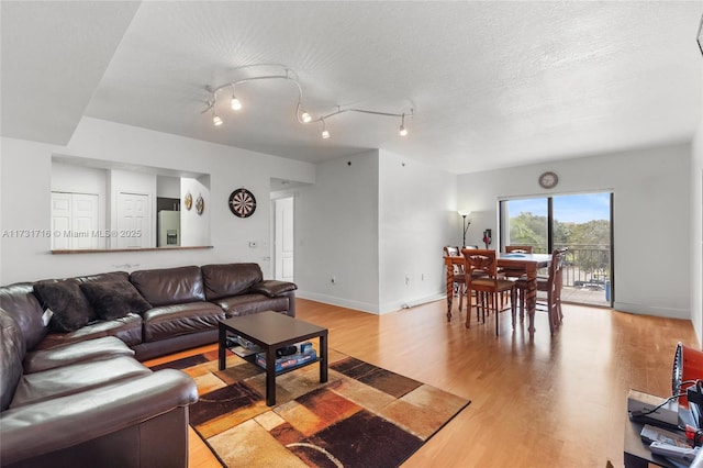 living room featuring light wood-style floors, track lighting, baseboards, and a textured ceiling