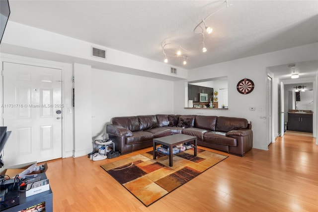 living room with light wood-type flooring, visible vents, and a textured ceiling