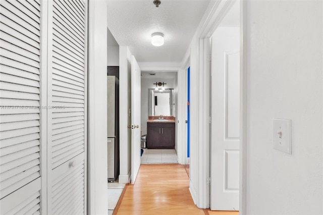 corridor featuring a sink, light wood-style flooring, and a textured ceiling