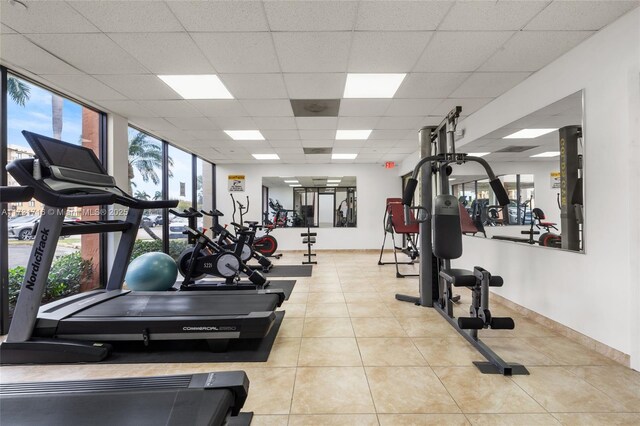 exercise room with light tile patterned floors, a drop ceiling, expansive windows, and plenty of natural light