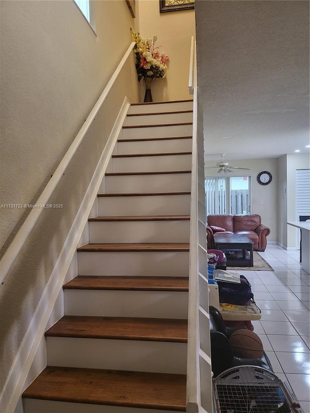 stairway with a textured ceiling, tile patterned floors, and ceiling fan