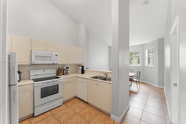 kitchen featuring cream cabinetry, light tile patterned floors, light countertops, a sink, and white appliances